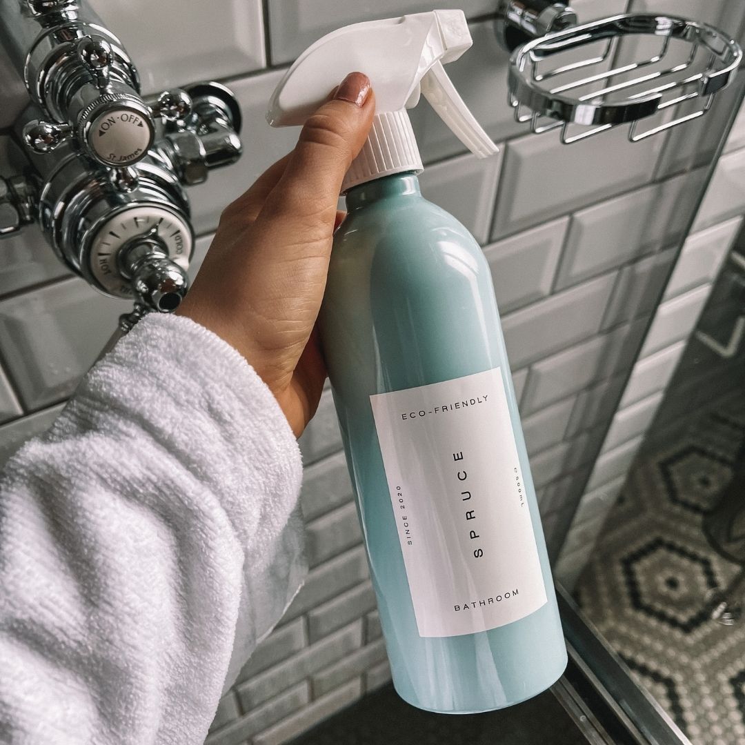 hand holding a shower cleaner spray in front of shower wall and taps
