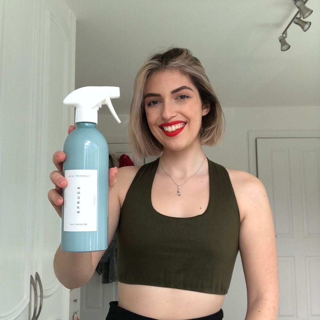 A smiling woman holding a blue shower cleaner spray