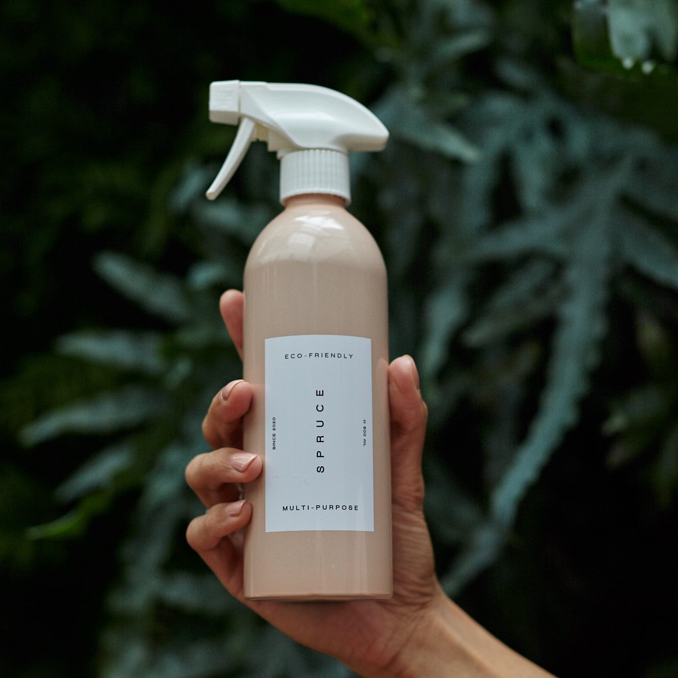 hand holding natural cleaning products spray bottle in front of dark green leaves