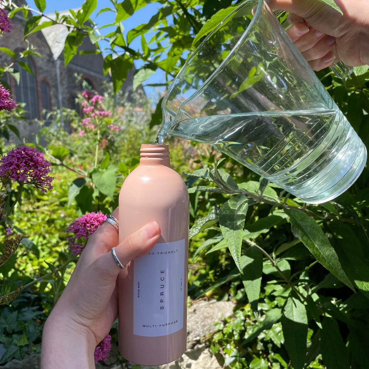 person refilling natural cleaning products with water in a garden